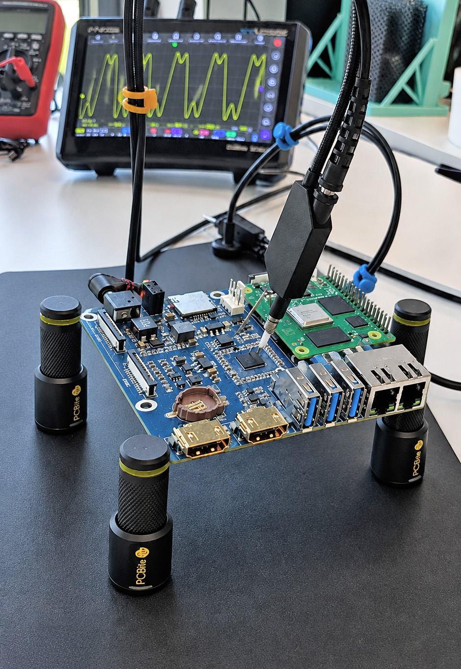 Circuit board under test probes, with an oscilloscope behind it
